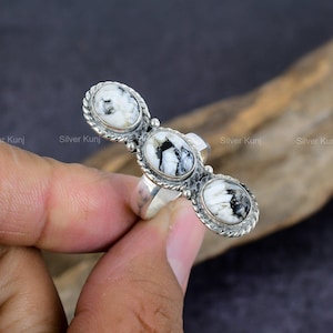 Può includere: Un anello d'argento con tre pietre ovali bianche e nere incastonate in una fascia d'argento. Le pietre sono disposte in fila, con la pietra centrale leggermente più grande delle altre due.