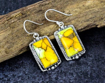 May include: A pair of rectangular earrings with a silver frame. The earrings have a vibrant yellow and green stone with a textured appearance. The frame has a twisted rope design and small silver beads. The earrings hang from a curved hook.