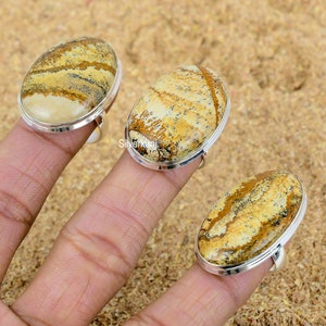 Puede incluir: Tres anillos de plata con engastes ovalados de piedras preciosas marrones y blancas. Los anillos están en un dedo.