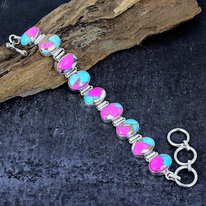 May include: A silver bracelet with pink and blue oval-shaped stones. The bracelet has a lobster clasp and a safety chain.