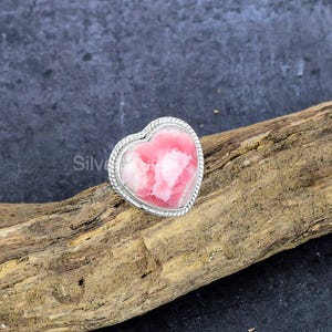Op de afbeelding: Een hartvormige ring met een roze en witte edelsteen gezet in een zilveren band.