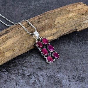May include: A silver pendant necklace featuring a cluster of oval-cut, deep red gemstones. The gemstones are set in a silver bezel setting and arranged in a vertical pattern. The necklace has a delicate silver chain.