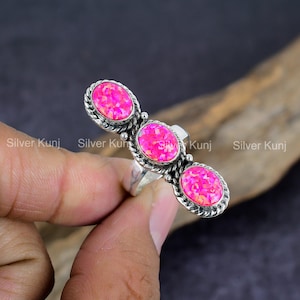 May include: A silver ring with three pink opal stones set in a row. The ring has a twisted band and a delicate design.
