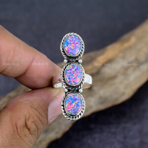 Puede incluir: Un anillo de plata con tres piedras preciosas de ópalo de forma ovalada. Los ópalos son una mezcla de rosa, morado y azul.