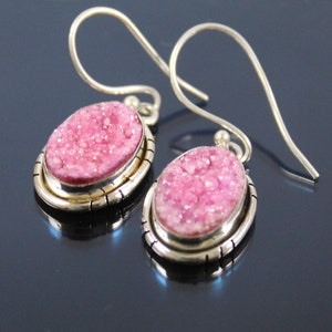 May include: A pair of silver dangle earrings with pink oval-shaped stones. The stones have a sparkly, textured surface.