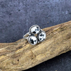 May include: A silver ring with three oval-shaped white and black stones set in a cluster. The stones are set in a silver bezel setting.