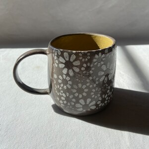 Peut inclure: Une tasse en céramique grise avec un motif floral blanc et un intérieur jaune.