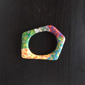 May include: A colorful, floral patterned bangle bracelet with a geometric shape. The bracelet is made of a hard, smooth material and has a bright, vibrant design.