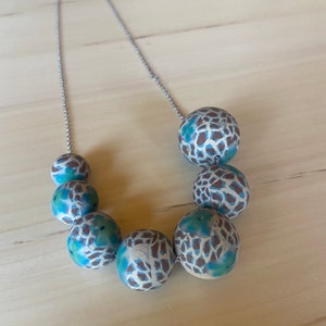 May include: A silver chain necklace with large, round, blue and white patterned beads. The beads have a brown and white animal print design.