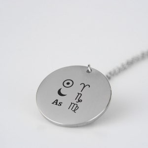 Pu&ograve; includere: Collana d'argento con un ciondolo rotondo che presenta simboli astrologici, tra cui il sole, la luna e i segni zodiacali Ariete, Scorpione e Capricorno. Il ciondolo include anche il testo "As".