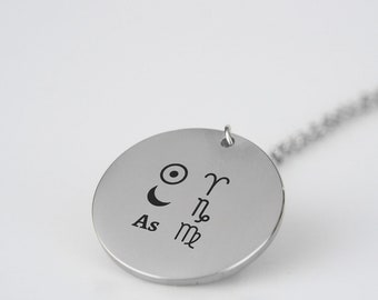 May include: Silver necklace with a round pendant featuring astrological symbols, including the sun, moon, and zodiac signs Aries, Scorpio, and Capricorn. The pendant also includes the text "As".