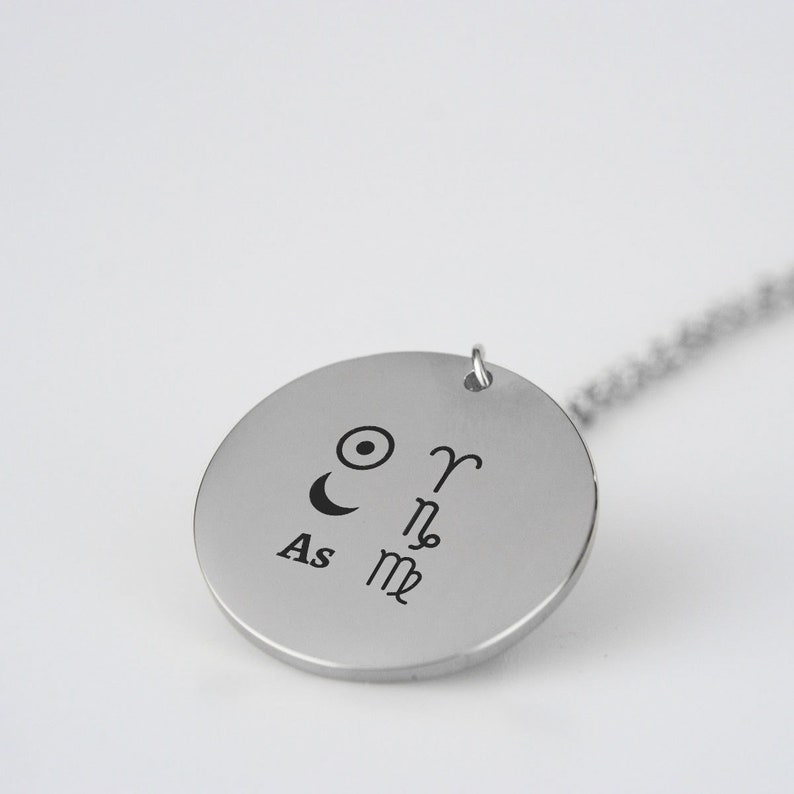 Pu&ograve; includere: Collana d'argento con un ciondolo rotondo che presenta simboli astrologici, tra cui il sole, la luna e i segni zodiacali Ariete, Scorpione e Capricorno. Il ciondolo include anche il testo "As".