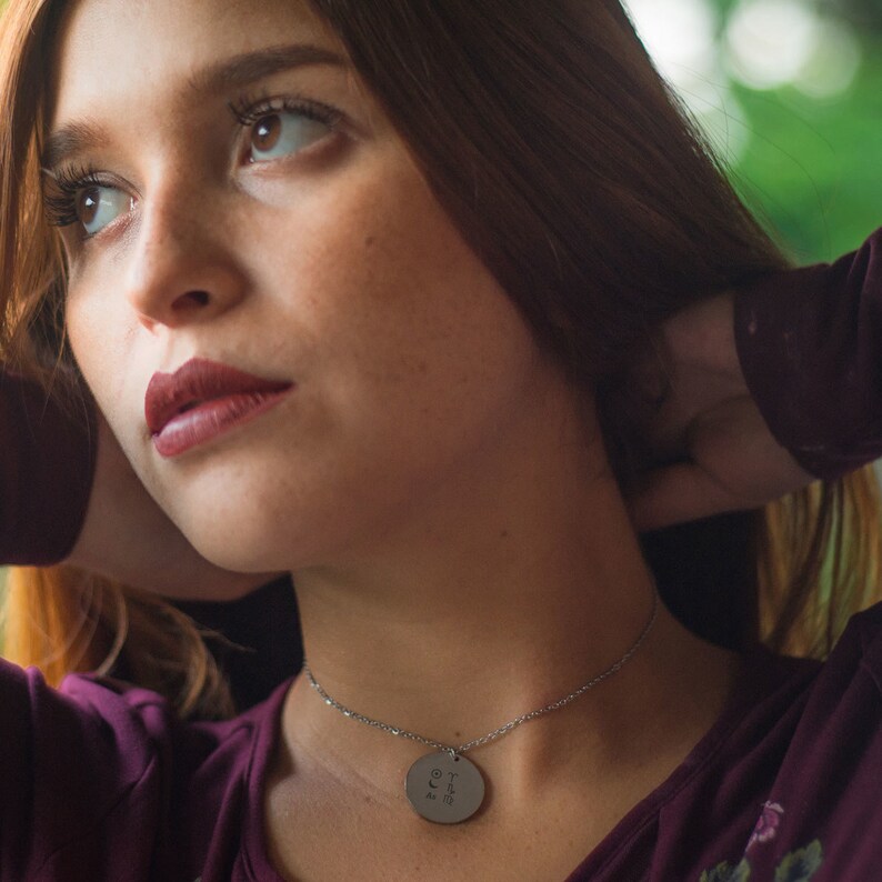 Pu&ograve; includere: Una donna con lunghi capelli castani indossa una camicia color granata con una collana d'argento e un ciondolo rotondo. Il ciondolo ha la parola "forever" incisa.