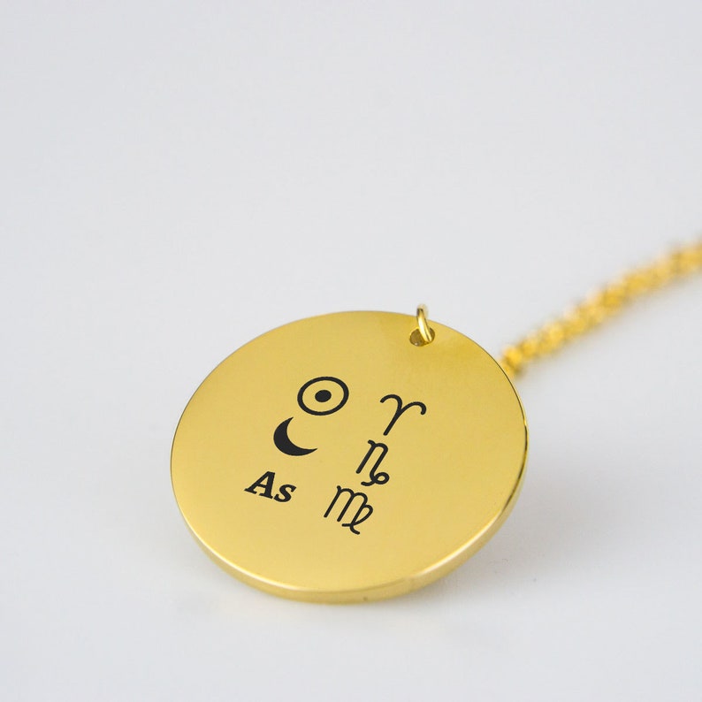 Pu&ograve; includere: Collana d'oro con un ciondolo rotondo che presenta simboli astrologici, tra cui il sole, la luna e i segni zodiacali Ariete, Sagittario e Scorpione. Il ciondolo include anche il testo "As".