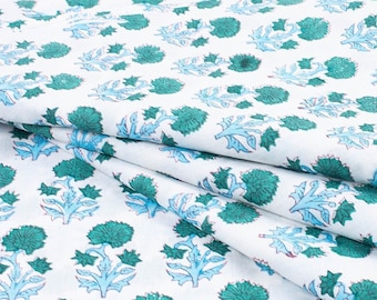 May include: White fabric with a repeating pattern of blue and green stylized flowers. The fabric is folded in a diagonal pattern.