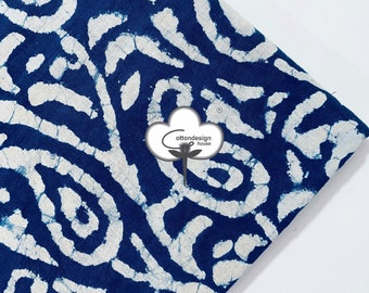Pode incluir: Um pedaço de tecido dobrado com um padrão abstrato azul e branco. O tecido tem um fundo azul escuro com um design branco e rodopiante. O logotipo "cottondesign house" é visível no canto inferior direito.