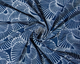 May include: Blue and white fabric with a repeating pattern of stylized seashells. The fabric is folded and draped, showing the texture and detail of the print.