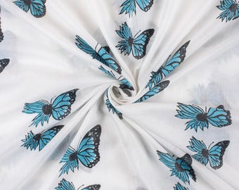 May include: White fabric with a repeating pattern of blue and black butterflies. The butterflies have detailed wing patterns and are scattered across the fabric. The fabric is gathered in a swirl, creating folds and shadows.