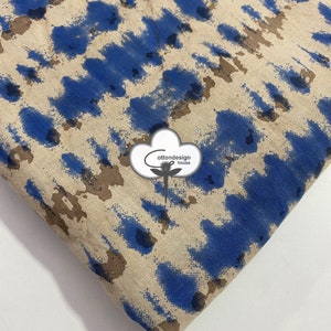 Puede incluir: Tela beige con un estampado abstracto azul y marrón. La tela tiene una superficie ligeramente texturizada. La tela está doblada en la esquina inferior derecha. El texto "cottondesign house" es visible en el centro de la imagen.