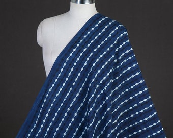 May include: A bolt of indigo blue fabric draped over a mannequin. The fabric features a repeating pattern of white dotted lines against a dark blue background. The fabric is likely cotton or a similar material, suitable for clothing or home decor.