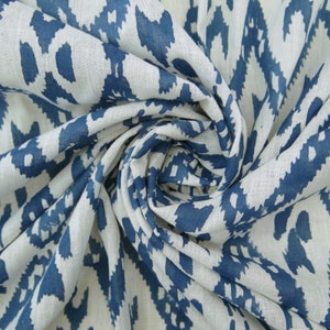 May include: Close-up of a white fabric with a repeating blue ikat pattern. The fabric is tightly swirled, showing the texture and design. The pattern consists of irregular, elongated shapes in a zig-zag arrangement.