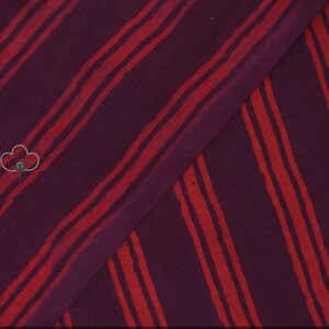May include: A piece of fabric with a deep purple background and bold, uneven red stripes running diagonally across it. The stripes vary in width and spacing, creating a dynamic visual texture. The fabric is folded, showing the pattern's continuity.