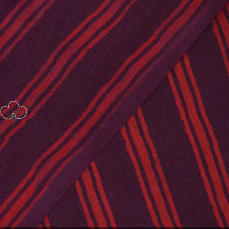 May include: A piece of fabric with a deep purple background and bold, uneven red stripes running diagonally across it. The stripes vary in width and spacing, creating a dynamic visual texture. The fabric is folded, showing the pattern's continuity.