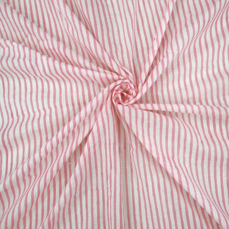 May include: Pink and white striped fabric with a wavy pattern. The fabric is folded and draped.