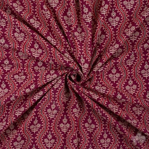 Könnte beinhalten: Nahaufnahme eines burgunderfarbenen Stoffes mit einem weißen Blumenmuster. Der Stoff ist gefaltet und hat ein wirbelndes Design.
