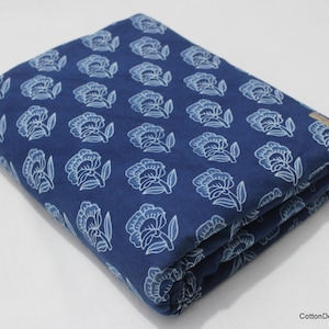 Könnte beinhalten: Ein gefaltetes Stück blauer Baumwollstoff mit einem weißen Blumenmuster. Der Stoff ist dreifach gefaltet und hat ein weißes Etikett in der oberen rechten Ecke.