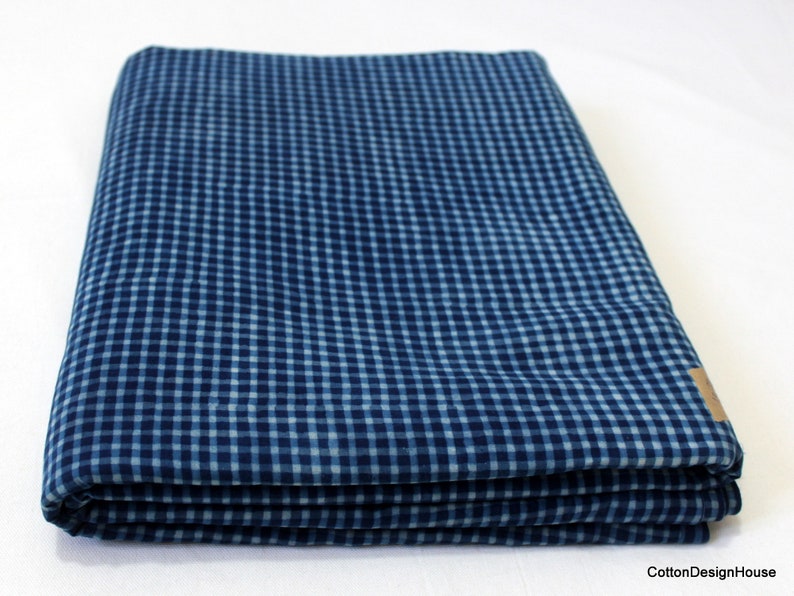 May include: A folded blue and white gingham fabric. The fabric has a checkered pattern.