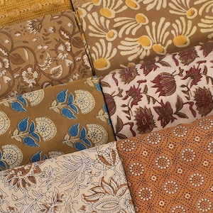 May include: Assortment of fabric swatches featuring various floral and geometric patterns in shades of brown, beige, and blue. The fabrics are arranged in a layered display, showcasing the intricate details of each design.