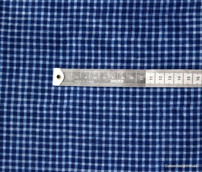 May include: Blue and white gingham fabric with a ruler measuring 16 inches. The fabric has a subtle texture and a slightly faded look.