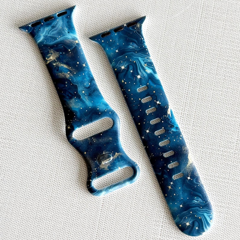 May include: A blue and gold galaxy print Apple Watch band. The band is made of silicone and has a sporty design.