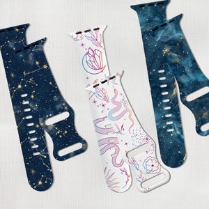 May include: Three different Apple Watch bands with celestial and nature-inspired designs. The first band features a dark blue background with gold constellations and stars. The second band has a white background with a colorful snake, crystals, and flowers. The third band has a dark blue and gold marble pattern.