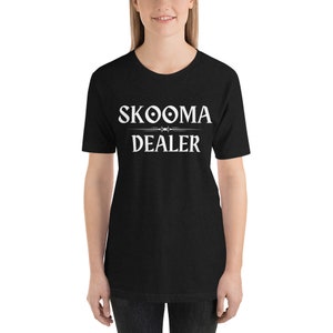 May include: Black t-shirt with white text that reads "SKOOMA DEALER" with a stylized symbol above the word "SKOOMA".