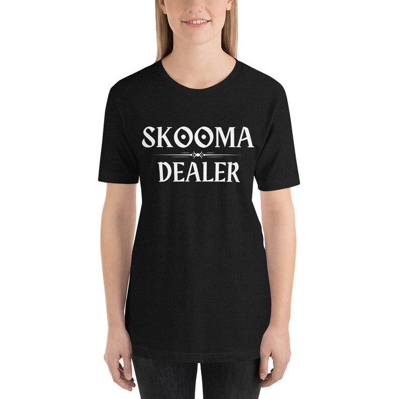 May include: Black t-shirt with white text that reads "SKOOMA DEALER" with a stylized symbol above the word "SKOOMA".