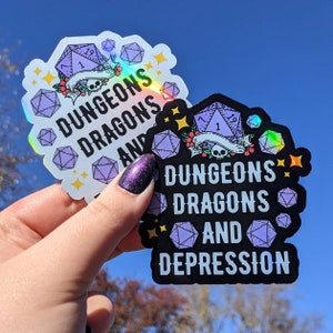 May include: Two holographic stickers with the text "DUNGEONS DRAGONS AND" and "DUNGEONS DRAGONS AND DEPRESSION". Each sticker features a purple D20 die, floral accents, and a banner. The background is a clear blue sky.