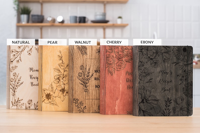 Peut inclure: Cinq livres de recettes en bois avec des motifs floraux et le texte "Mom's Recipe Book" dans diff&eacute;rentes teintes de bois&nbsp;: naturel, poire, noyer, cerisier et &eacute;b&egrave;ne.