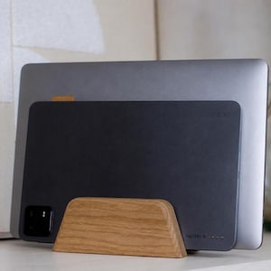 May include: A light-colored wooden stand holding a dark gray tablet and a larger silver laptop. The tablet features the text "xiaomi" in the bottom right corner and a black camera module in the bottom left corner, positioned upright in the wooden base.