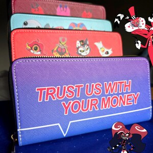 May include: A stack of zippered wallets in various colors, including purple, red, and teal. The purple wallet features the text "TRUST US WITH YOUR MONEY." Other wallets display cartoon character designs. The wallets are likely made of faux leather.