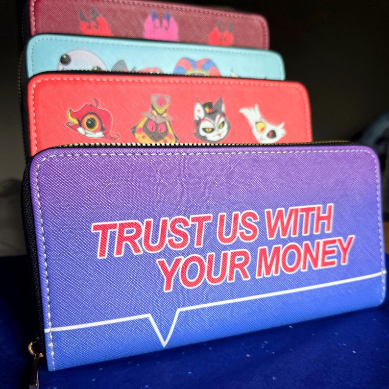 May include: A stack of zippered wallets in various colors. The front wallet is purple with the text "TRUST US WITH YOUR MONEY" in red. Other wallets are red, teal, and maroon, each with cartoon character designs.