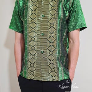 May include: A green and gold short-sleeved shirt with a traditional Thai pattern. The shirt has a mandarin collar and a button-up front.