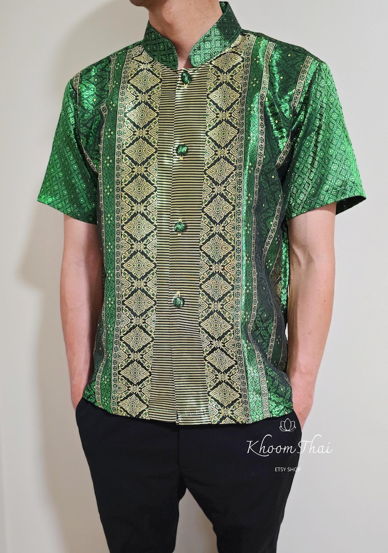 May include: A green and gold short-sleeved shirt with a traditional Thai pattern. The shirt has a mandarin collar and a button-up front.