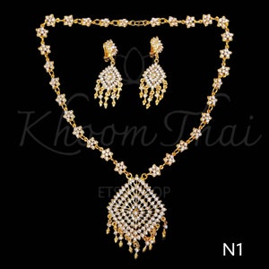 May include: A gold necklace and earrings set with a large, ornate pendant and dangling earrings. The jewelry is adorned with clear rhinestones.