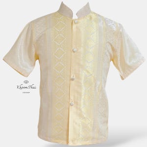 May include: A cream-coloured short-sleeved shirt with a mandarin collar and a button-up front. The shirt has a geometric pattern in a lighter shade of cream.