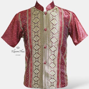 May include: A red and gold short-sleeved shirt with a mandarin collar and a button-up front. The shirt features a traditional Thai pattern.