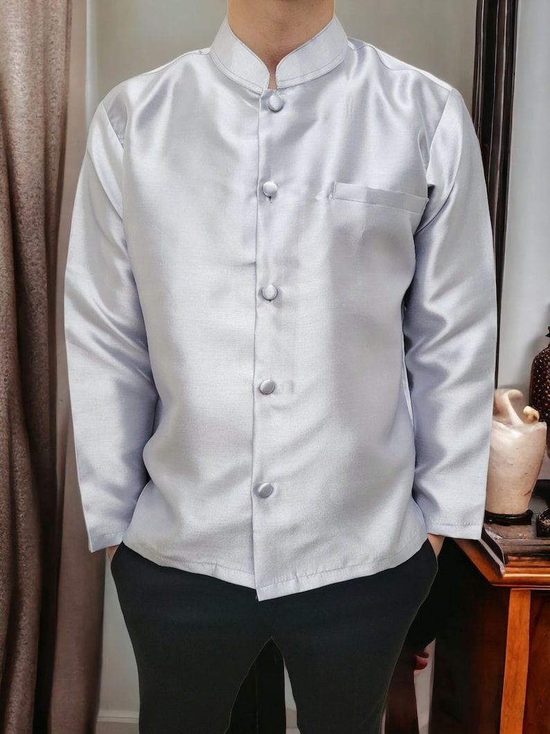 May include: A silver long-sleeved shirt with a mandarin collar and button fastening. The shirt has a pocket on the left side.