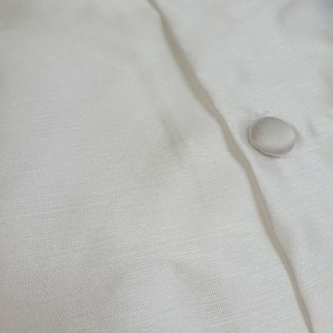 May include: Close-up of a white button-down shirt with two white buttons. The fabric has a subtle texture.
