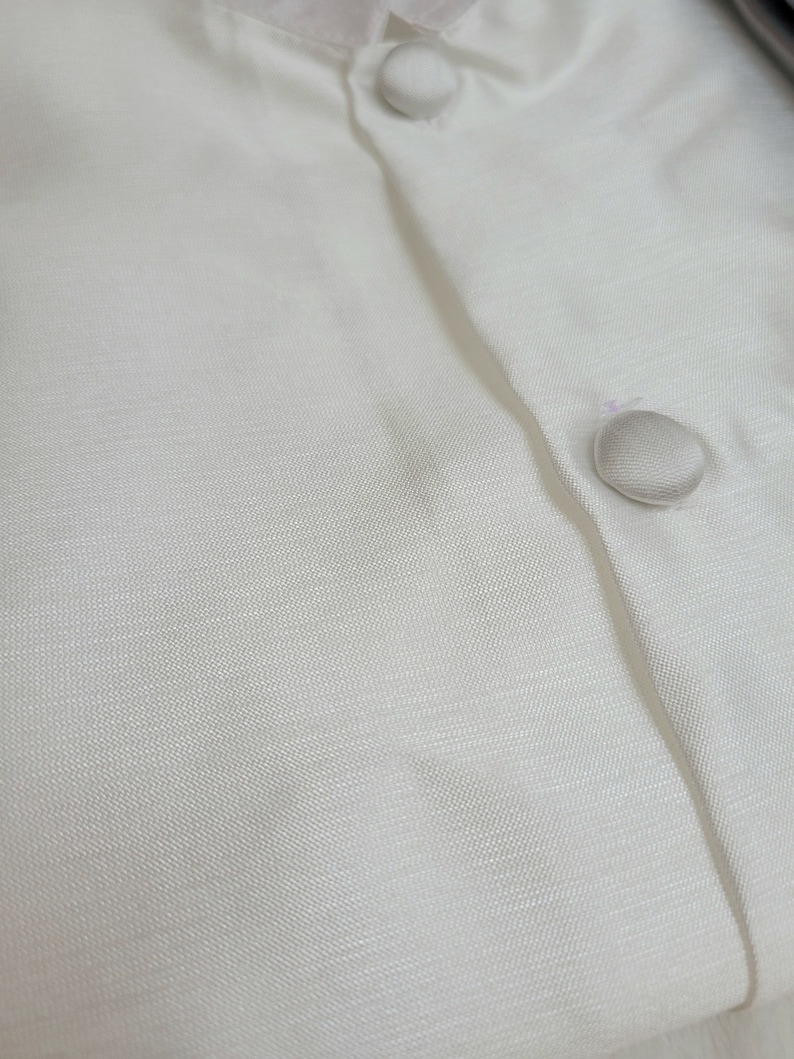May include: Close-up of a white button-down shirt with two white buttons. The fabric has a subtle texture.